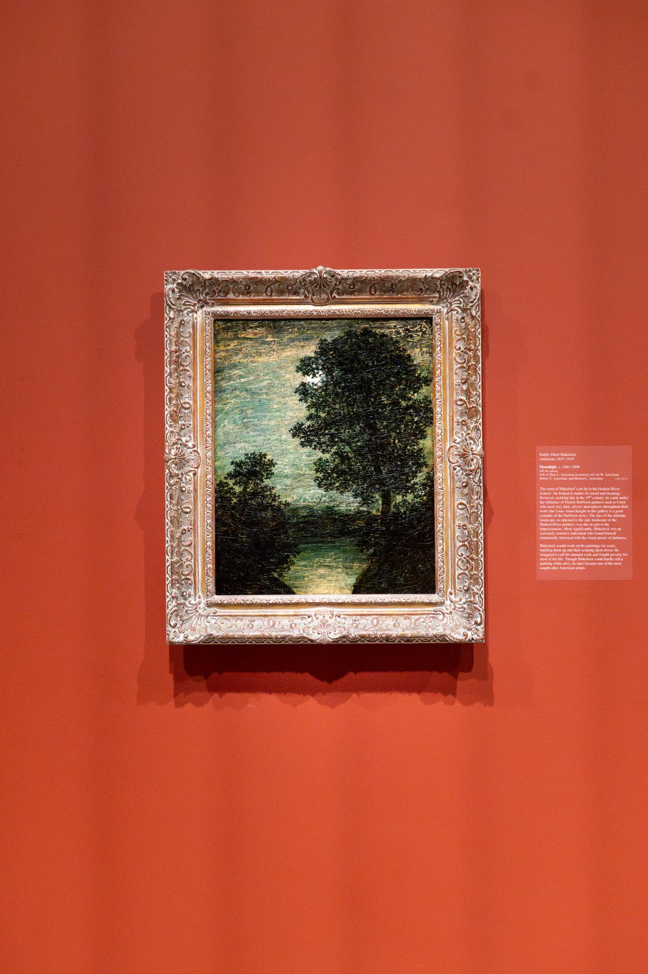 This small, dark painting of trees under the moon is surrounded with an ornate frame