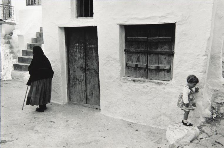 an older woman and a young child heading opposite directions in front of a white stone building