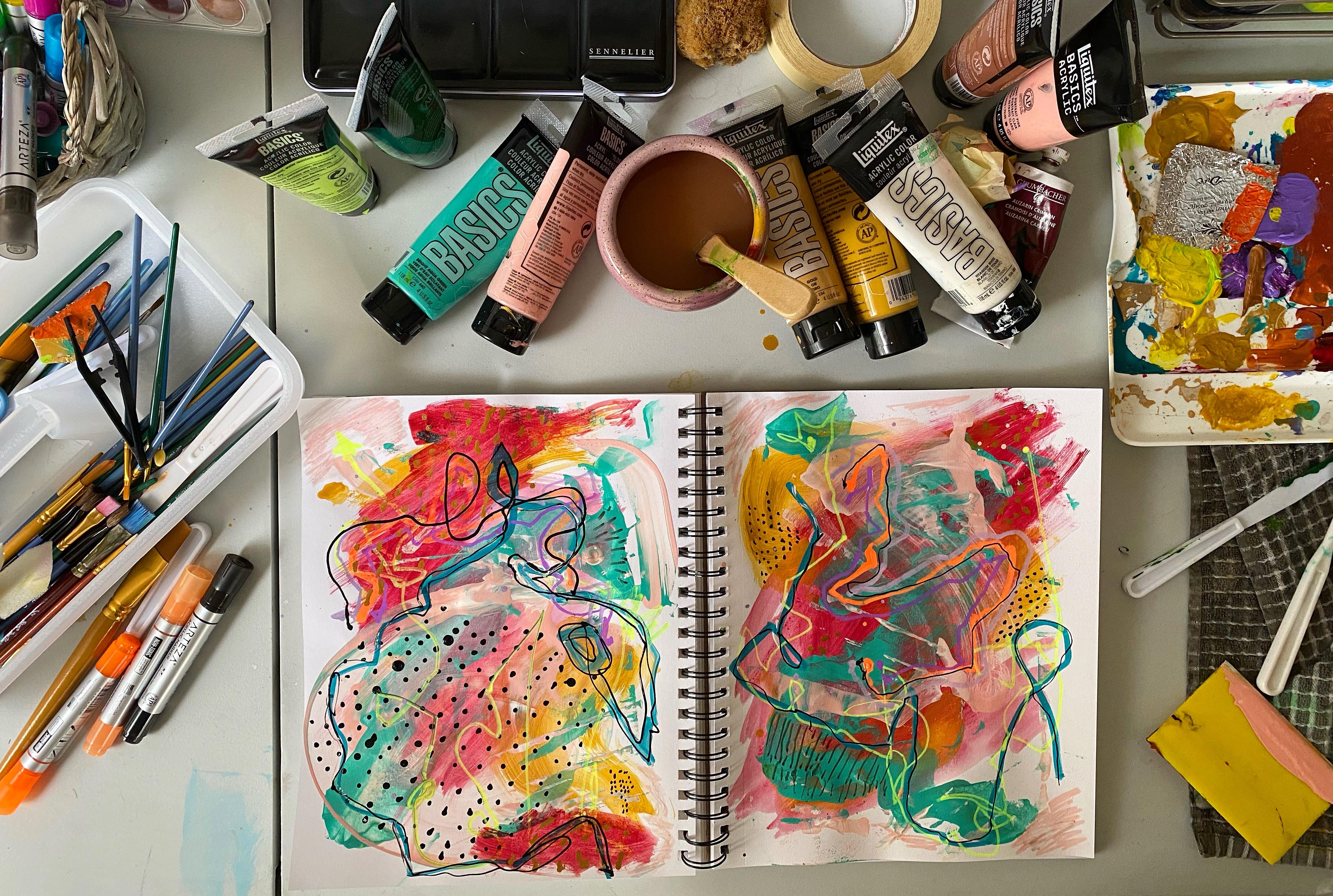 a messy and colorful journal surrounded by art supplies