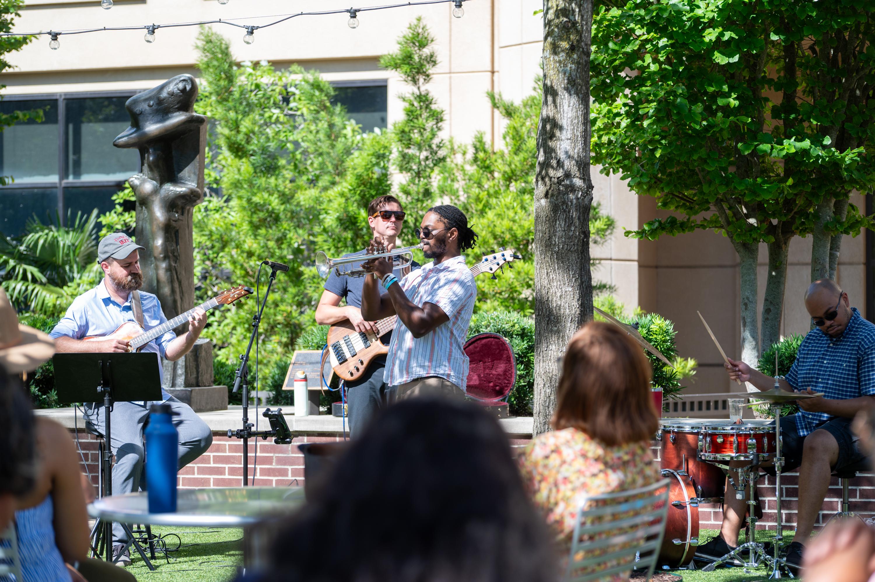 musicians playing on the plaza as an audience looks on from nearby tables