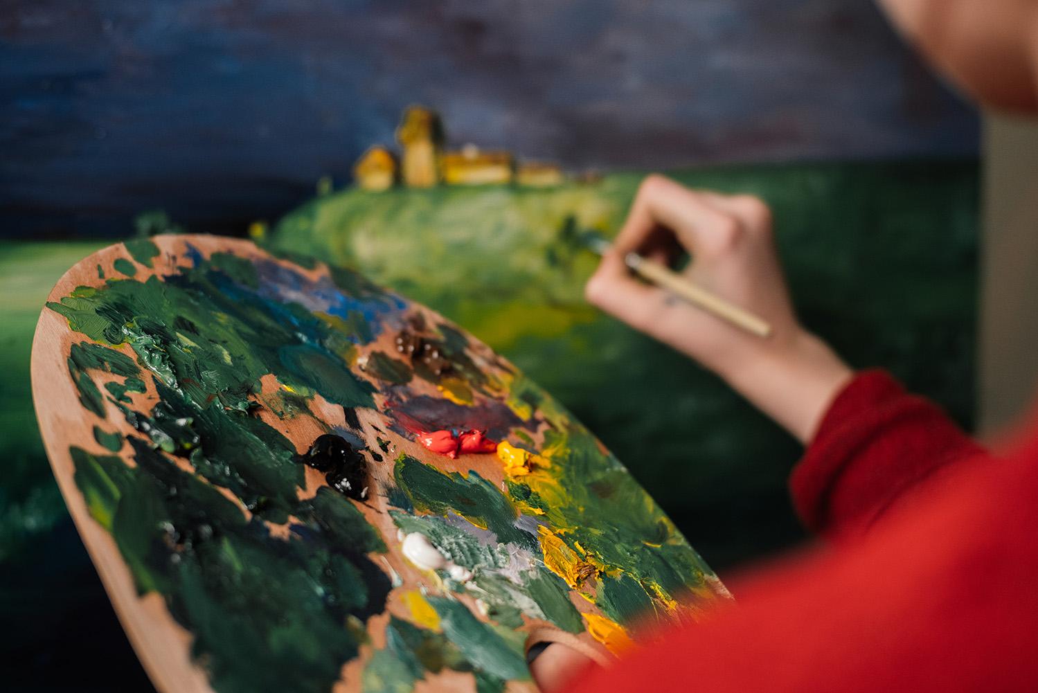 a student paints a landscape from mixed colors on a palate