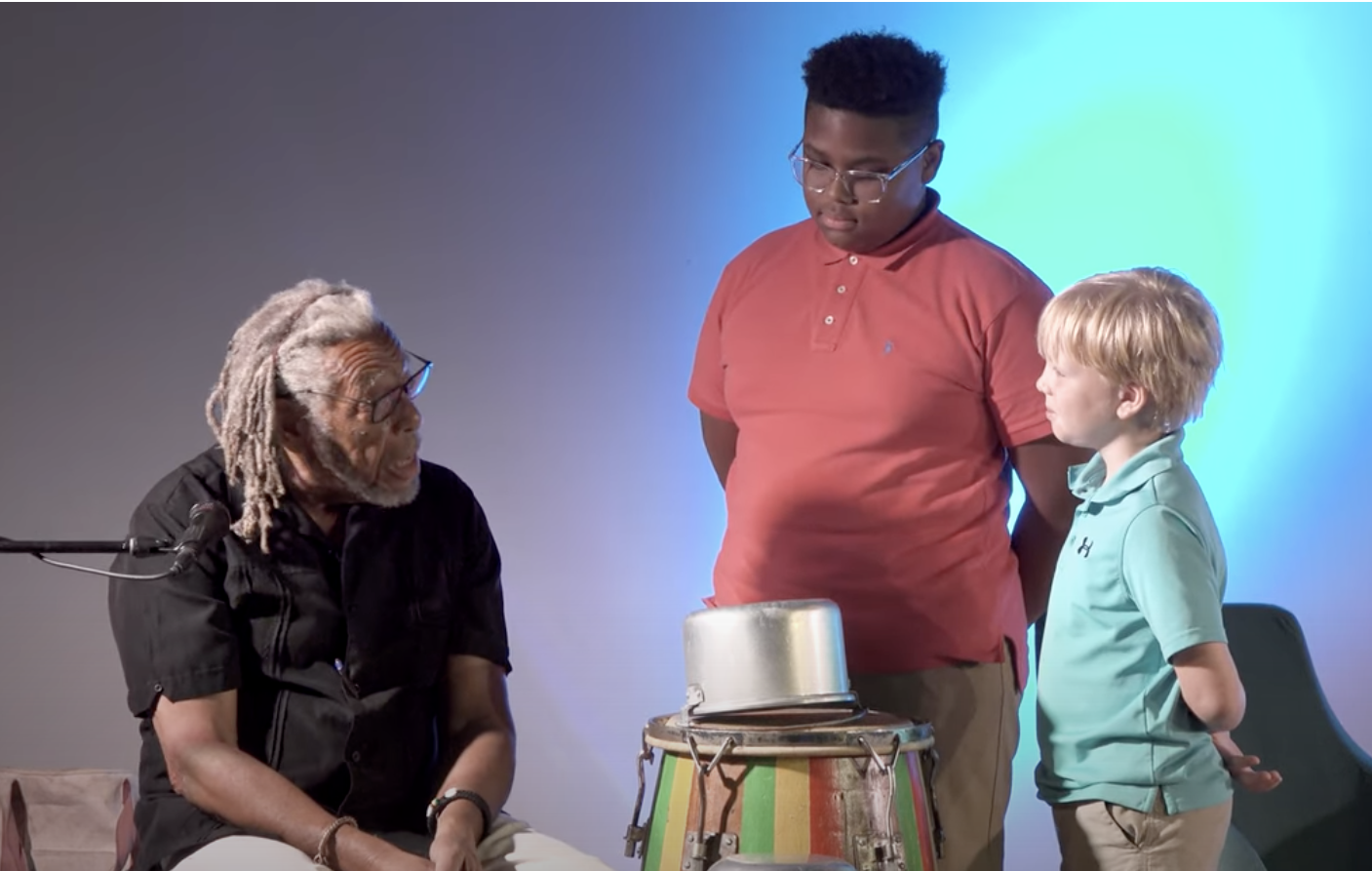 Two children and a man onstage around a drum